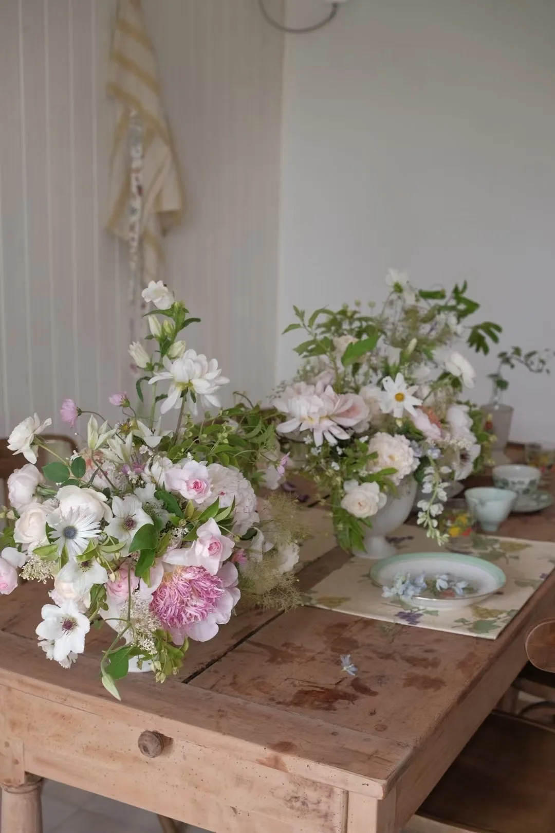 Two soft pink-and-white garden compotes on a rustic farmhouse table in a light-filled room
