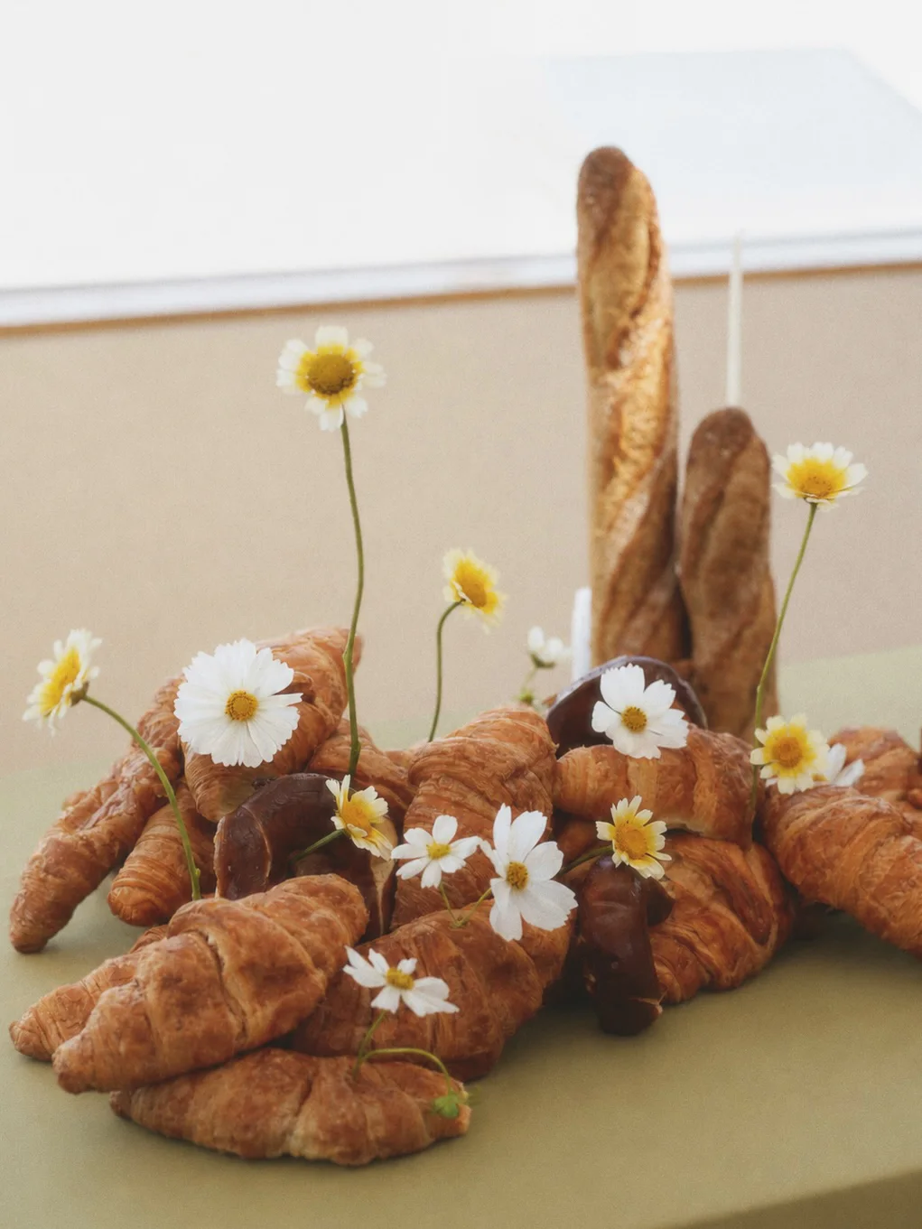 Croissants and rustic bread arranged beneath an upright baguette with airy white and yellow flowers