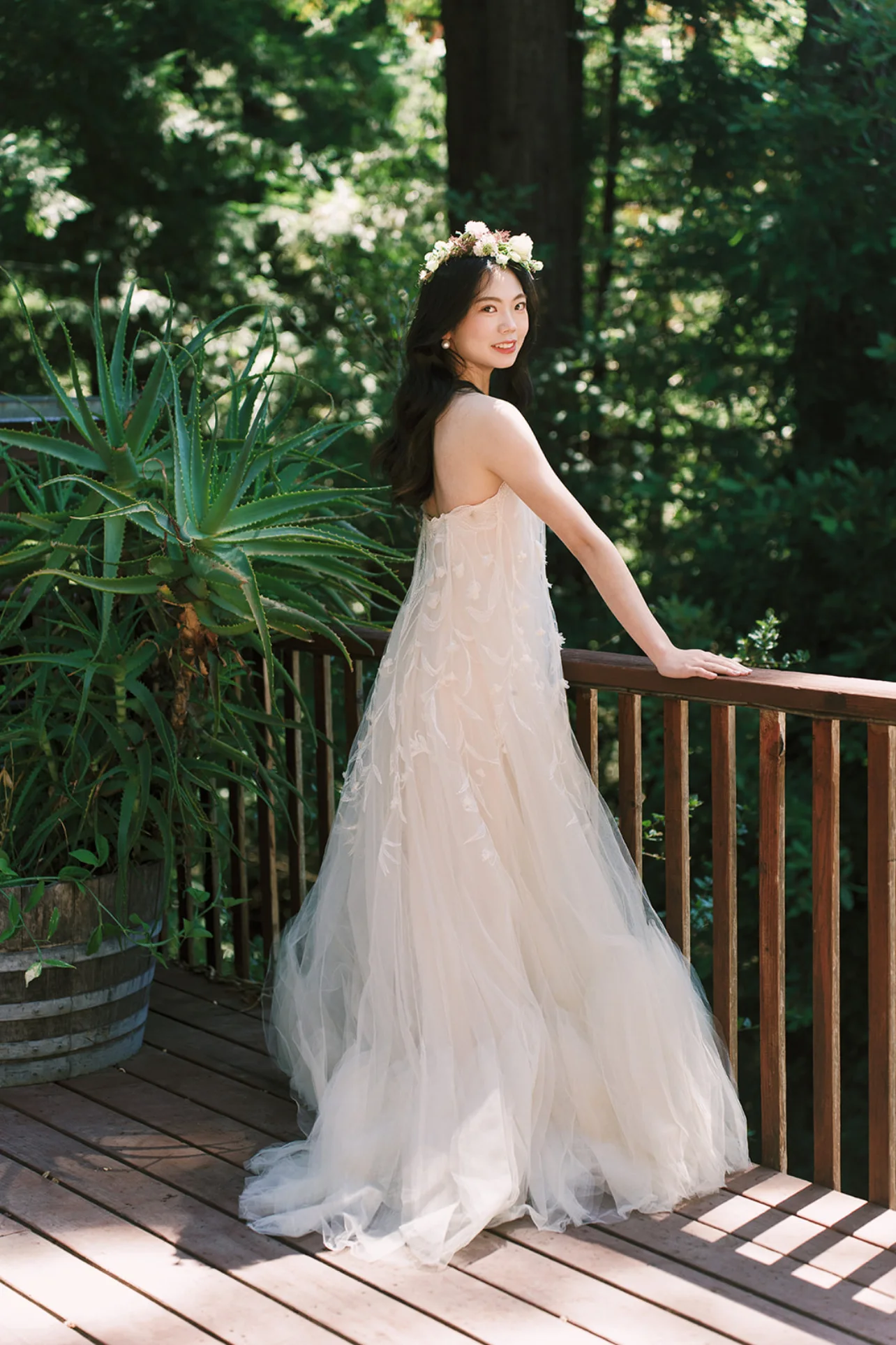 Bride wearing a delicate floral crown and an ivory gown on a wooden deck surrounded by greenery