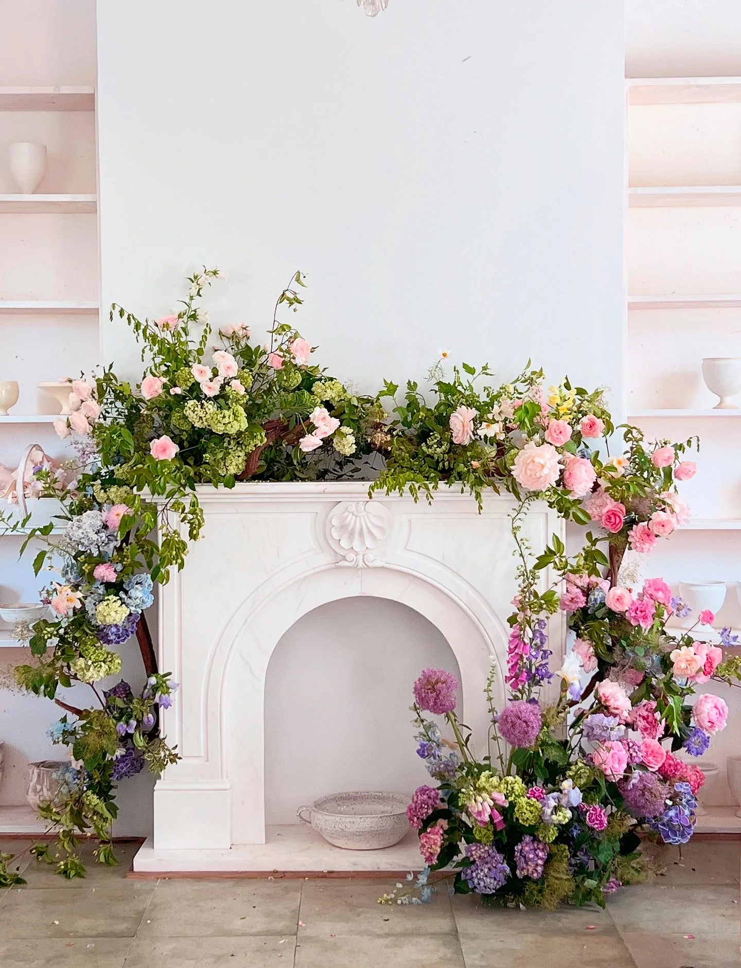 Blush and lavender floral installation framing a white marble mantel