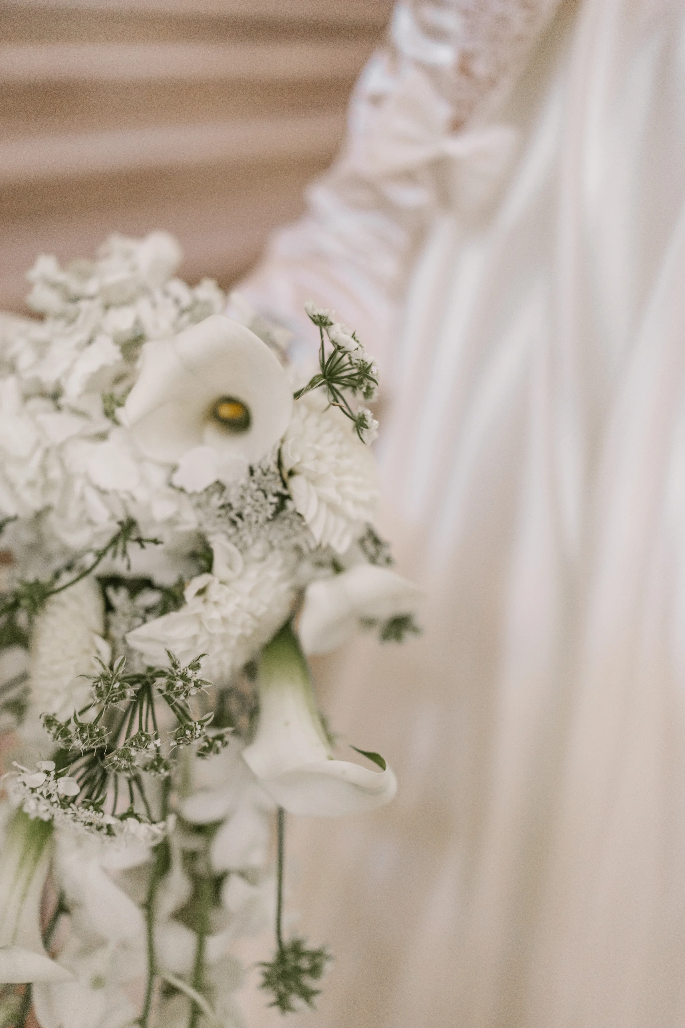 Close-up of a white calla lily and freesia bouquet against the satin gown