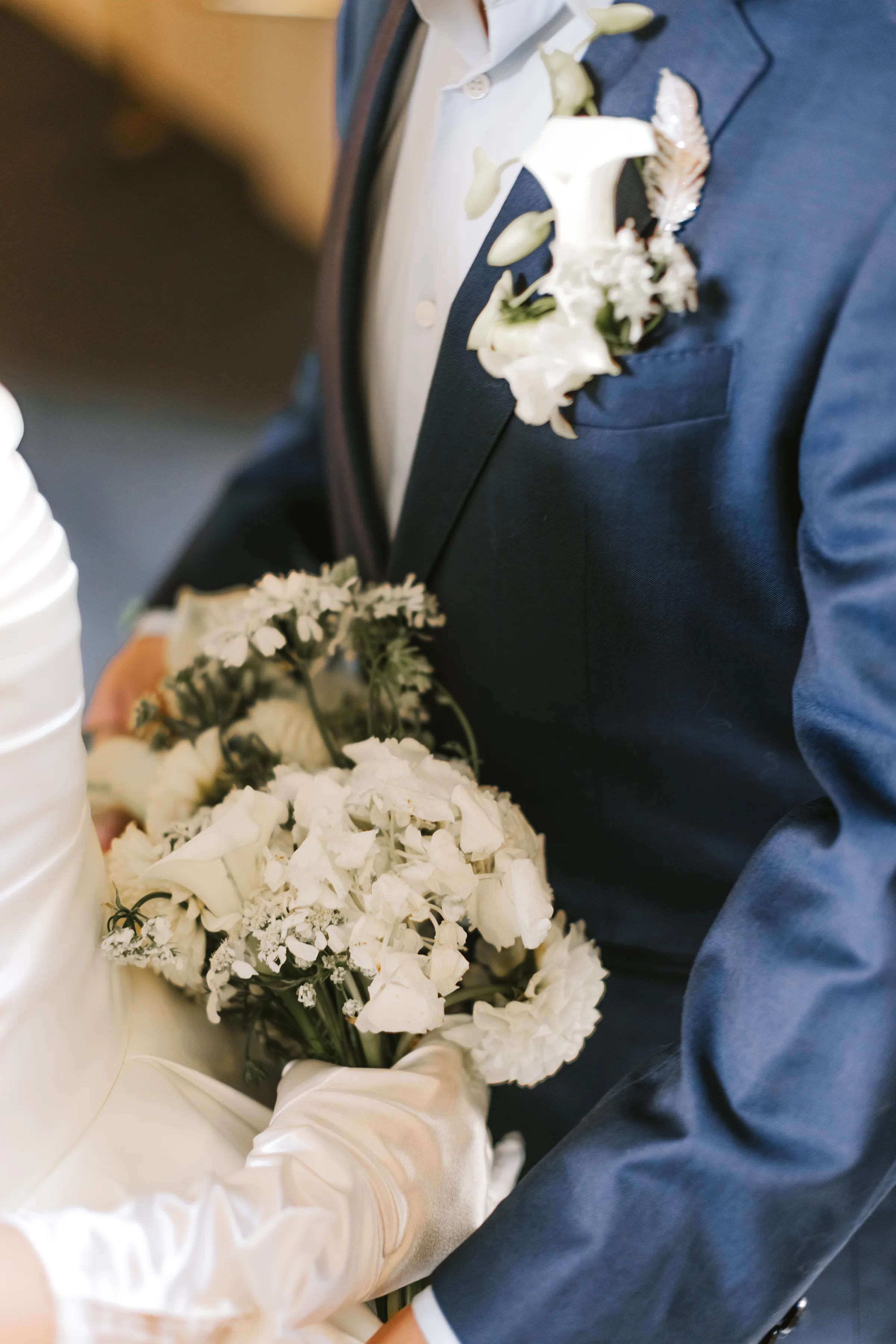 Bride's gloved hands holding a white bouquet beside the groom in a navy suit