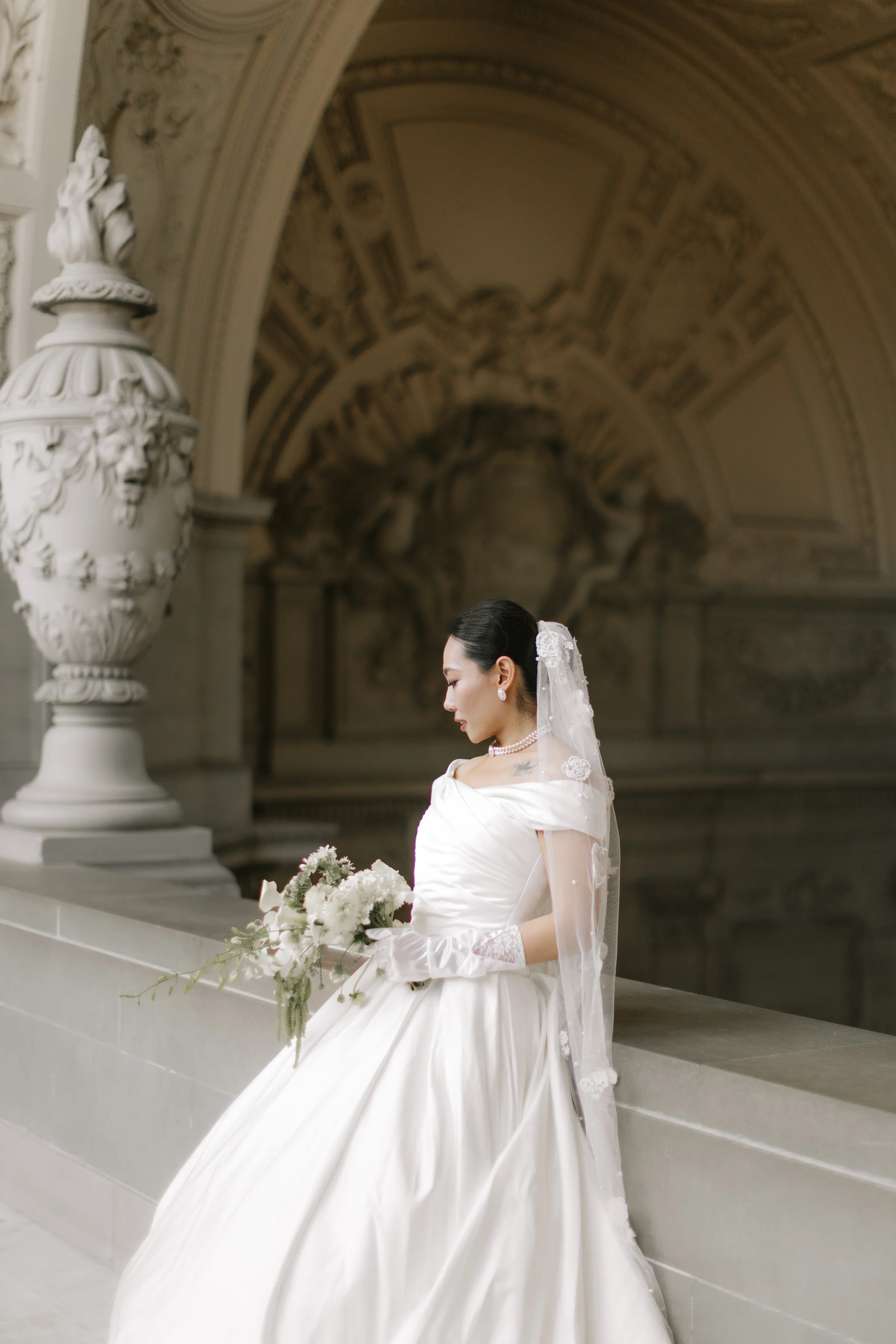 Bride beside an ornate marble urn holding her bouquet