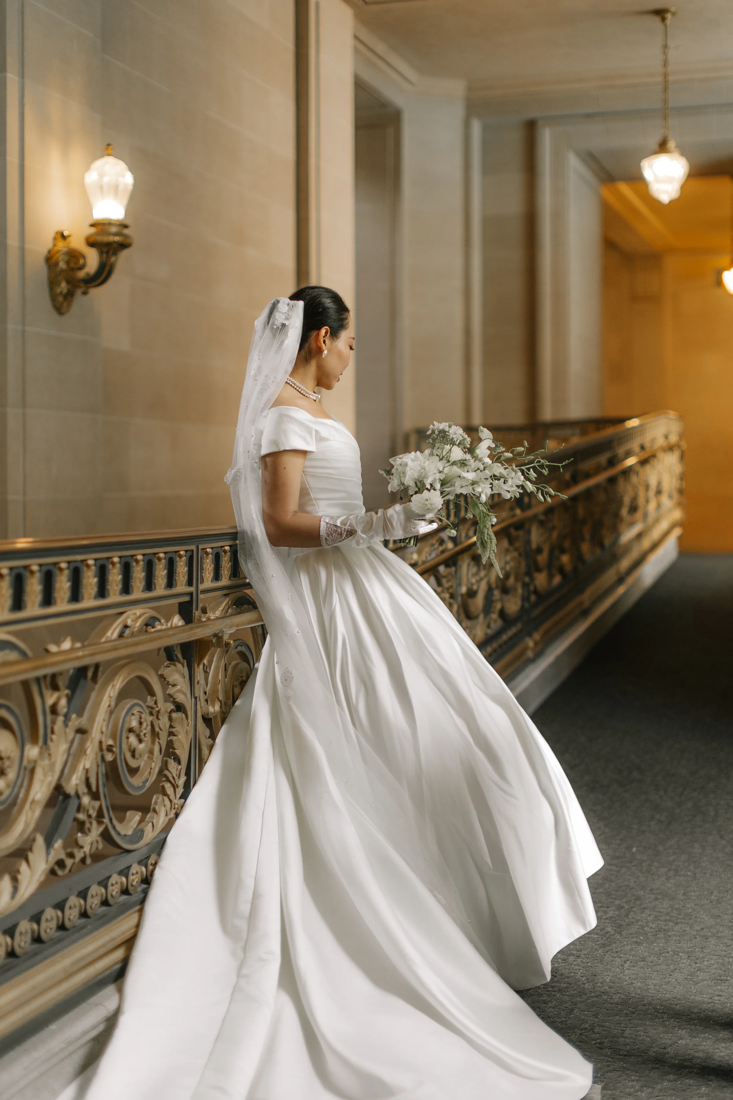 Bride turning on the staircase, her satin gown sweeping by the gilded railing