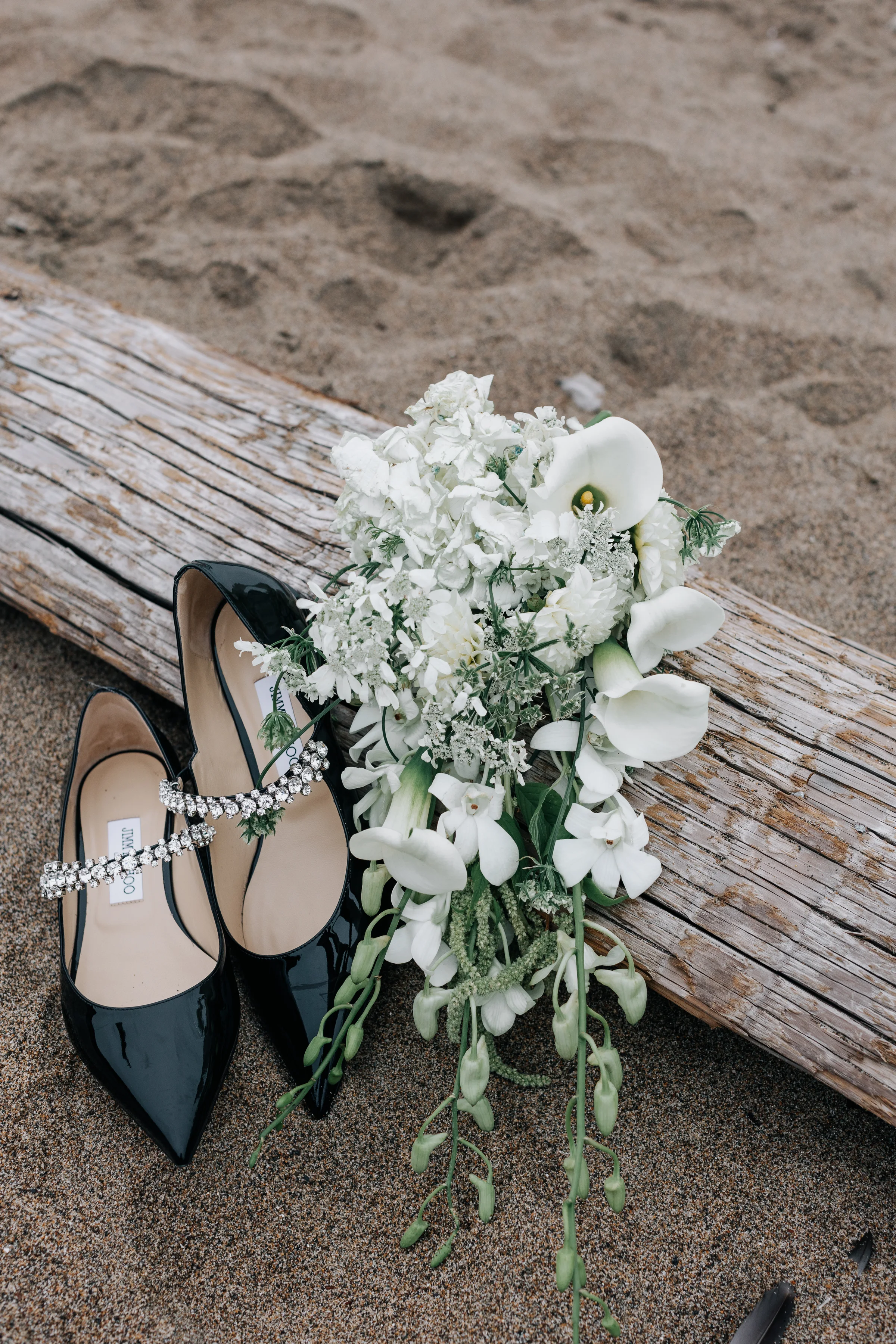Black bridal heels and a white bouquet resting on beach driftwood