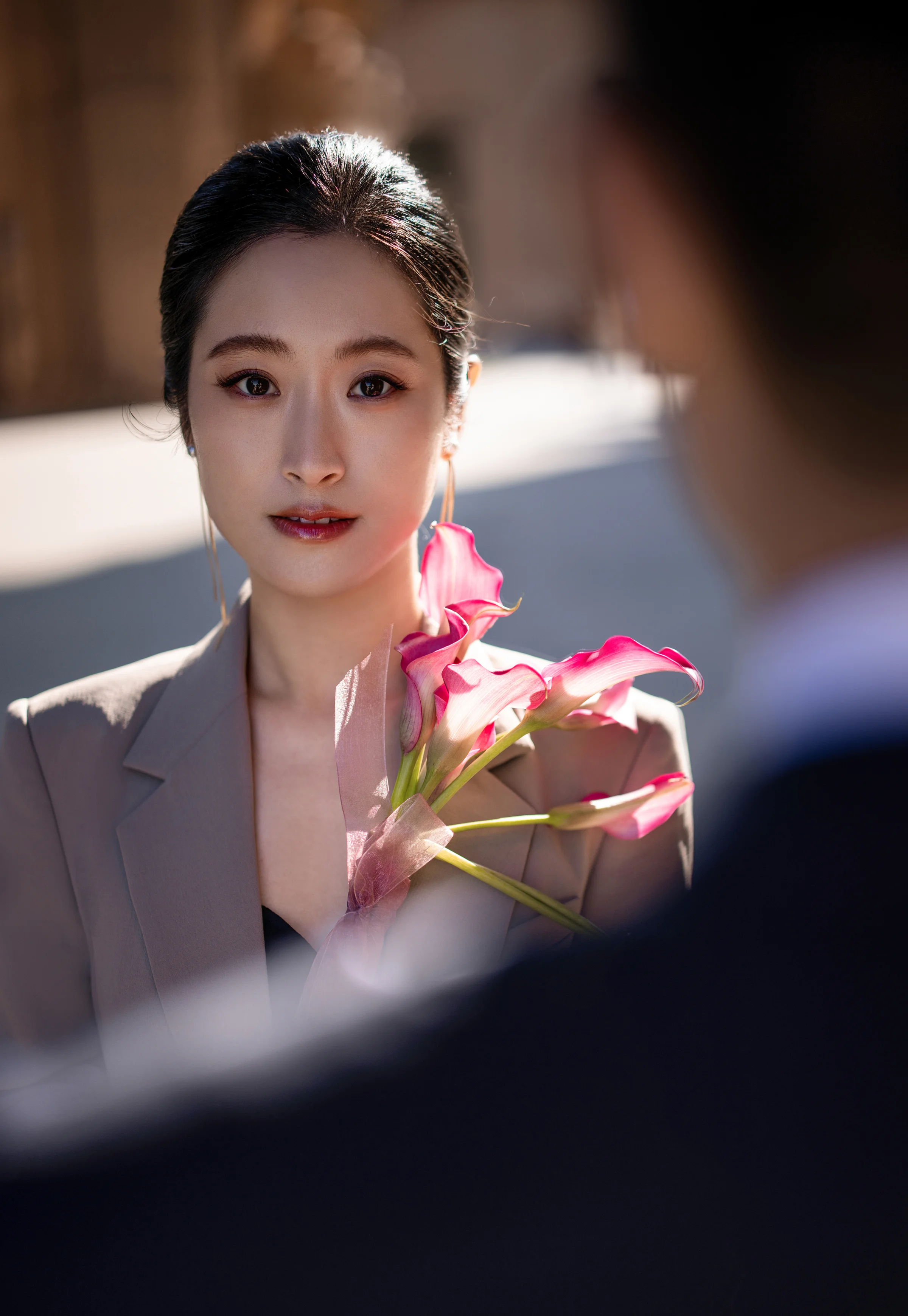 Portrait of the bride holding a pink orchid, the groom out of focus in the foreground