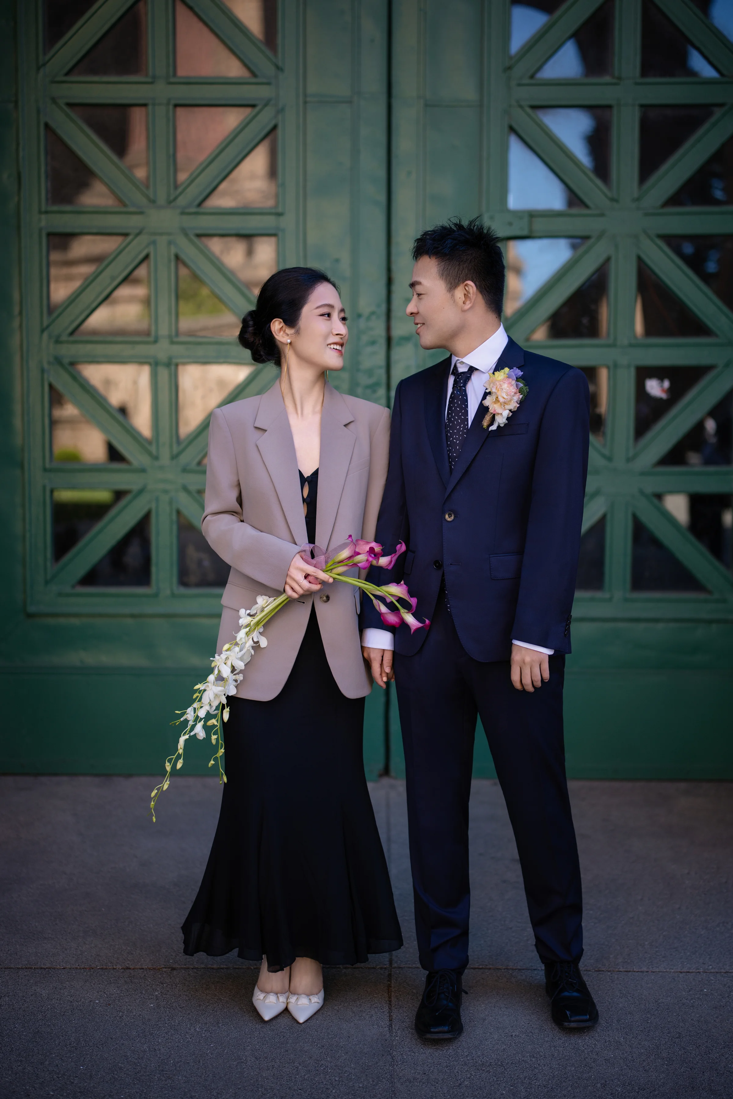 Couple portrait by a column, the bride in black holding a pink orchid stem