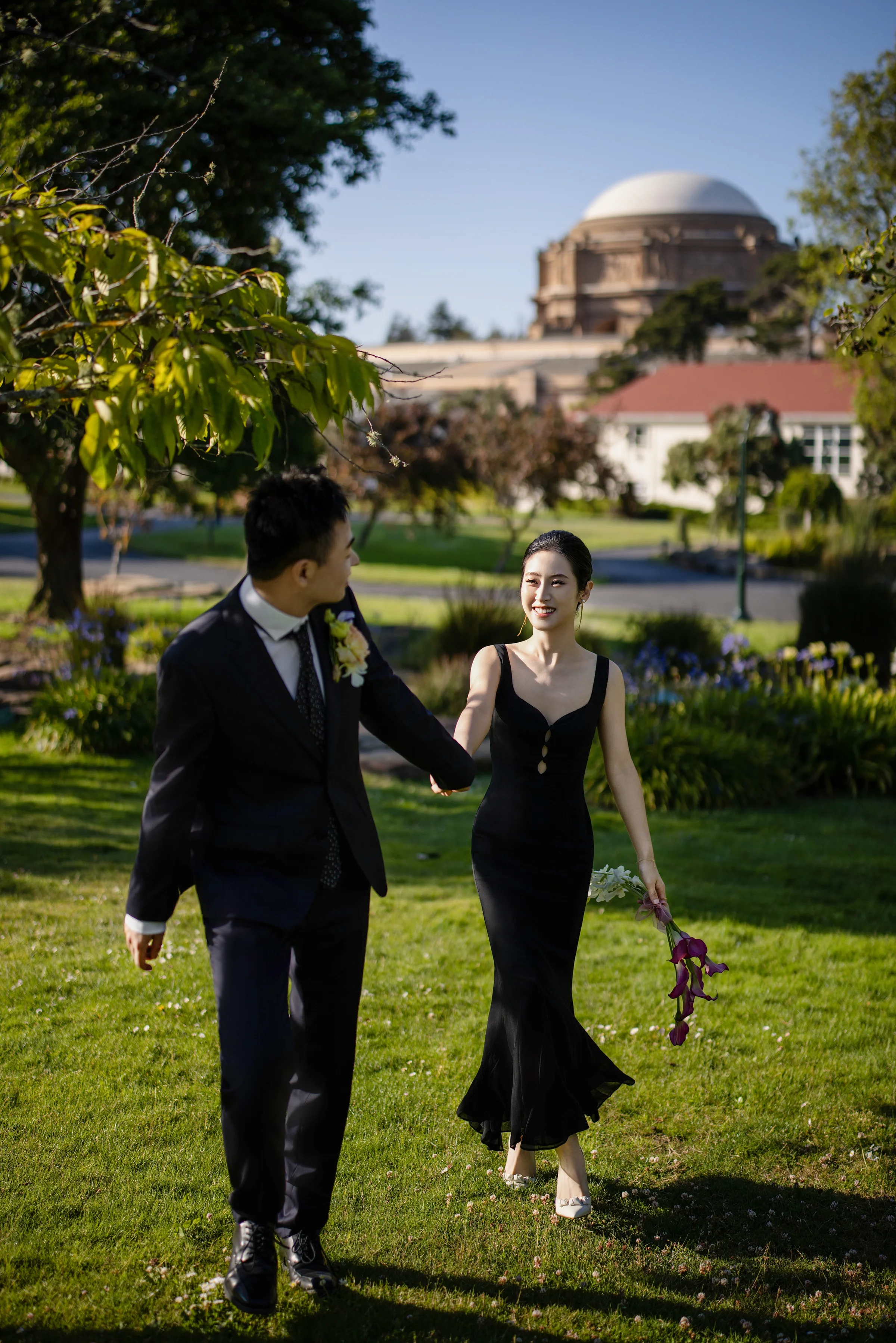 Couple before a teal geometric door, the bride in a blazer holding orchids