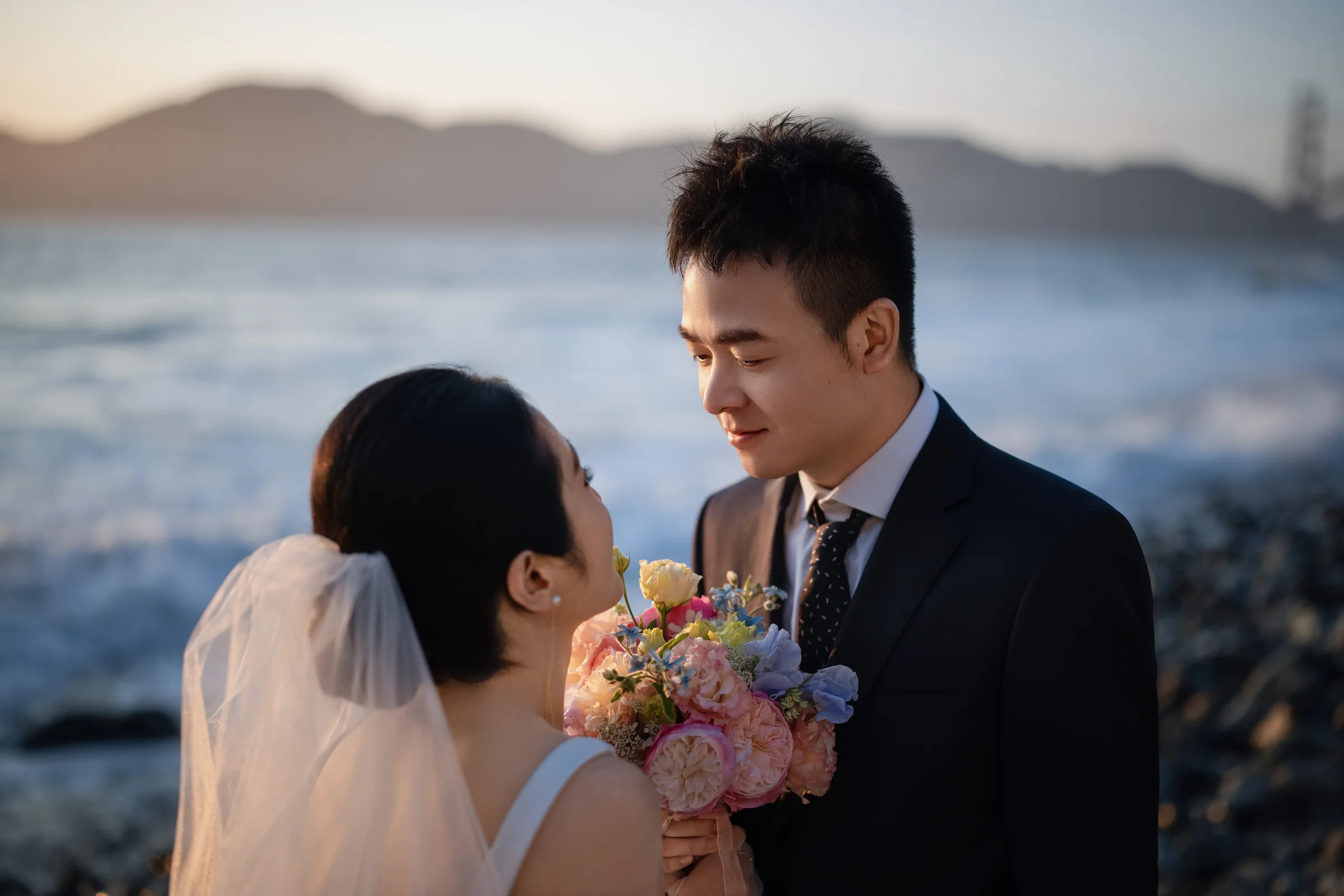 Couple close together at dusk, the bride holding a pastel bouquet