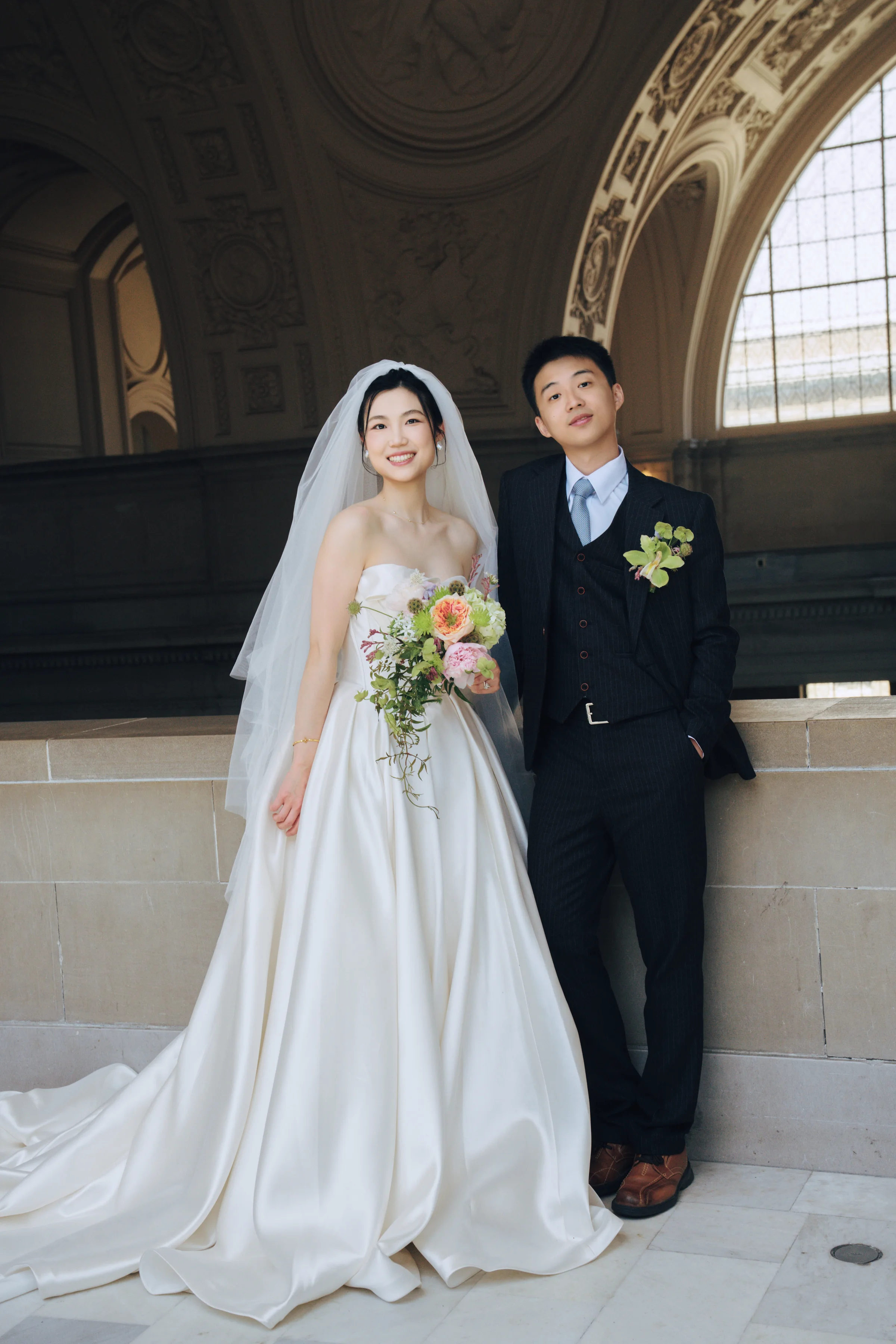 Couple beneath a grand arched window, the bride holding her bouquet