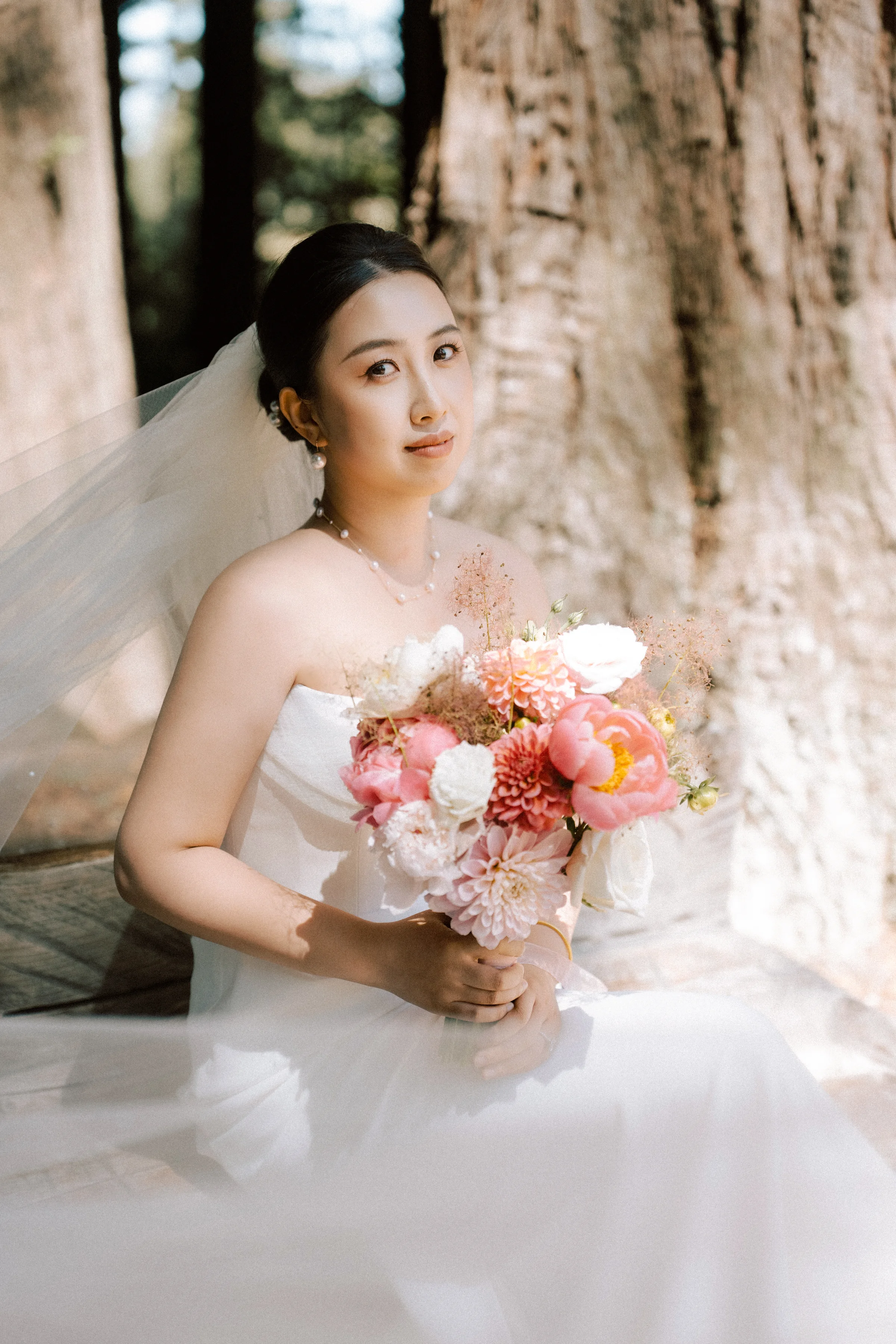 Bride seated holding a pink and coral bouquet among the redwoods