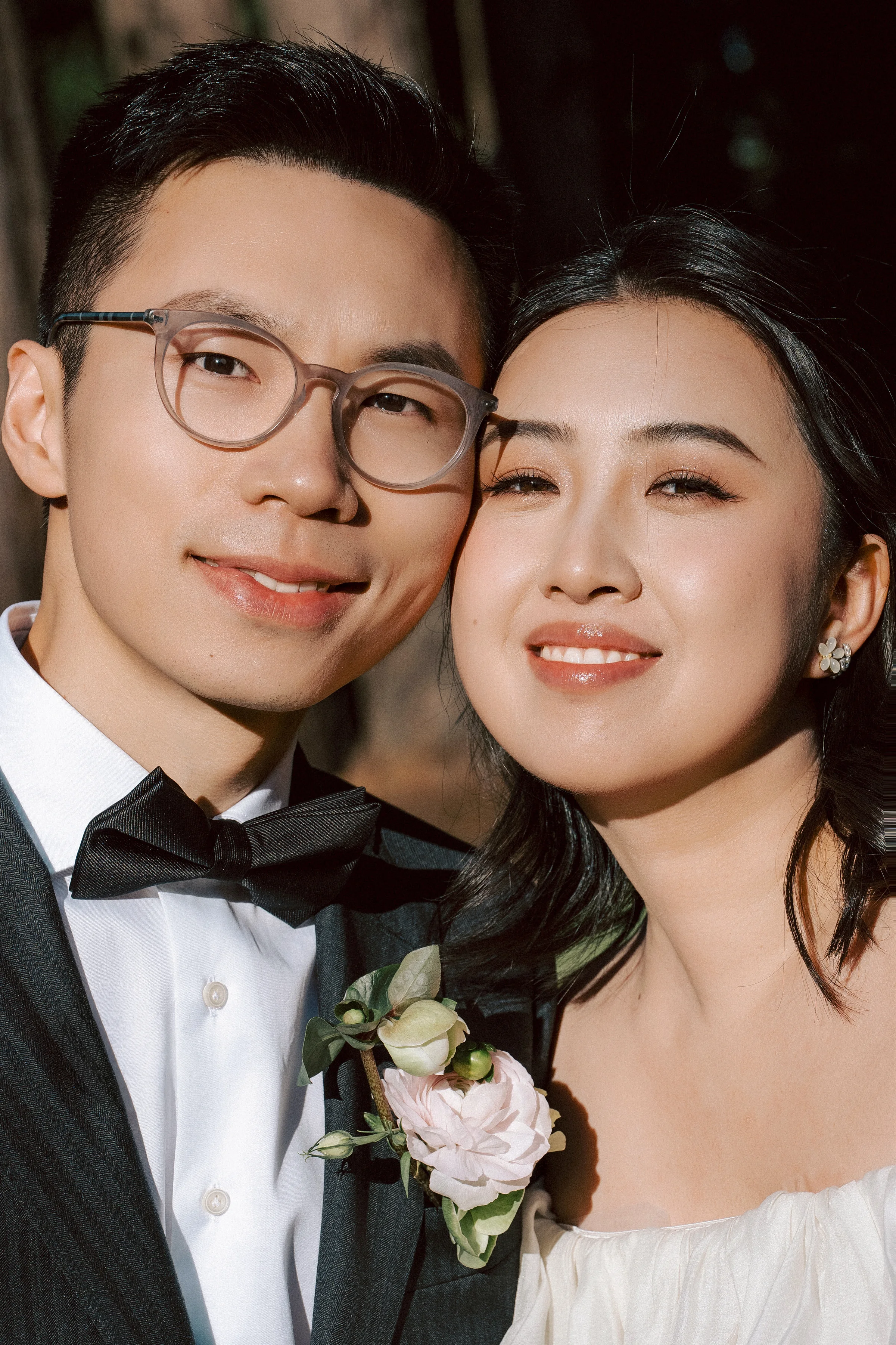 Close portrait of the couple, the groom in glasses and a bow tie, the bride in white