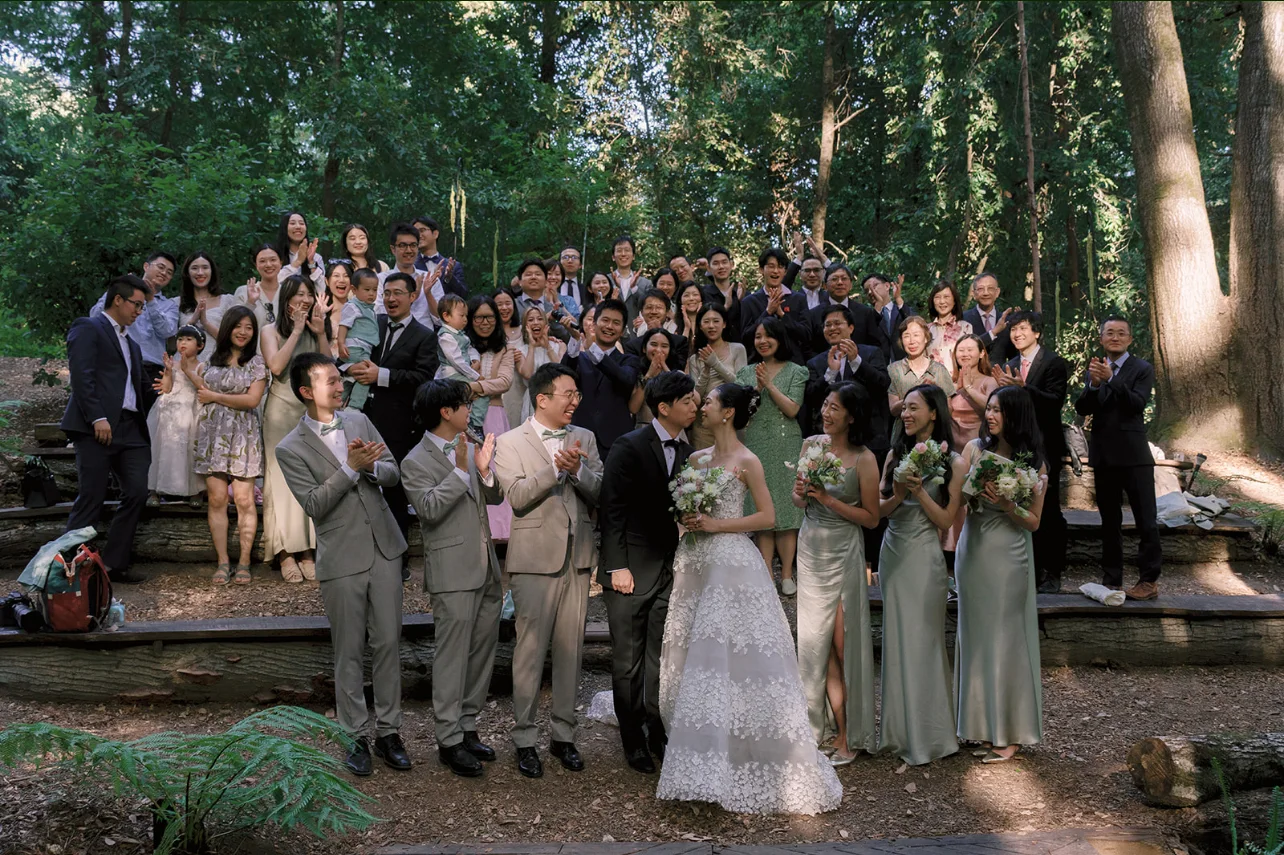 Newlyweds and their wedding party holding pastel bouquets in a large group portrait among the redwoods.