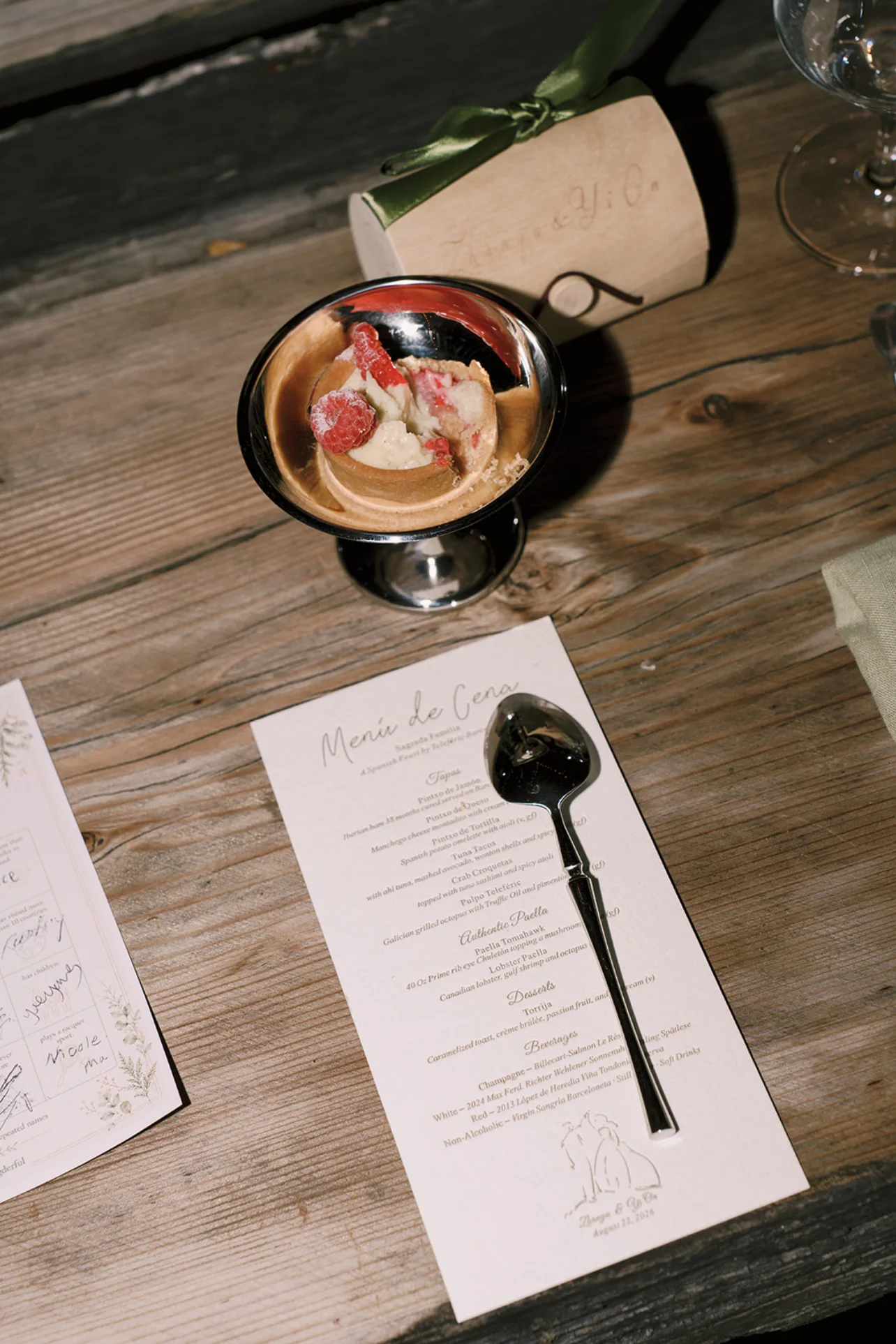 Raspberry dessert in a silver cup beside a printed dinner menu and guest place setting.