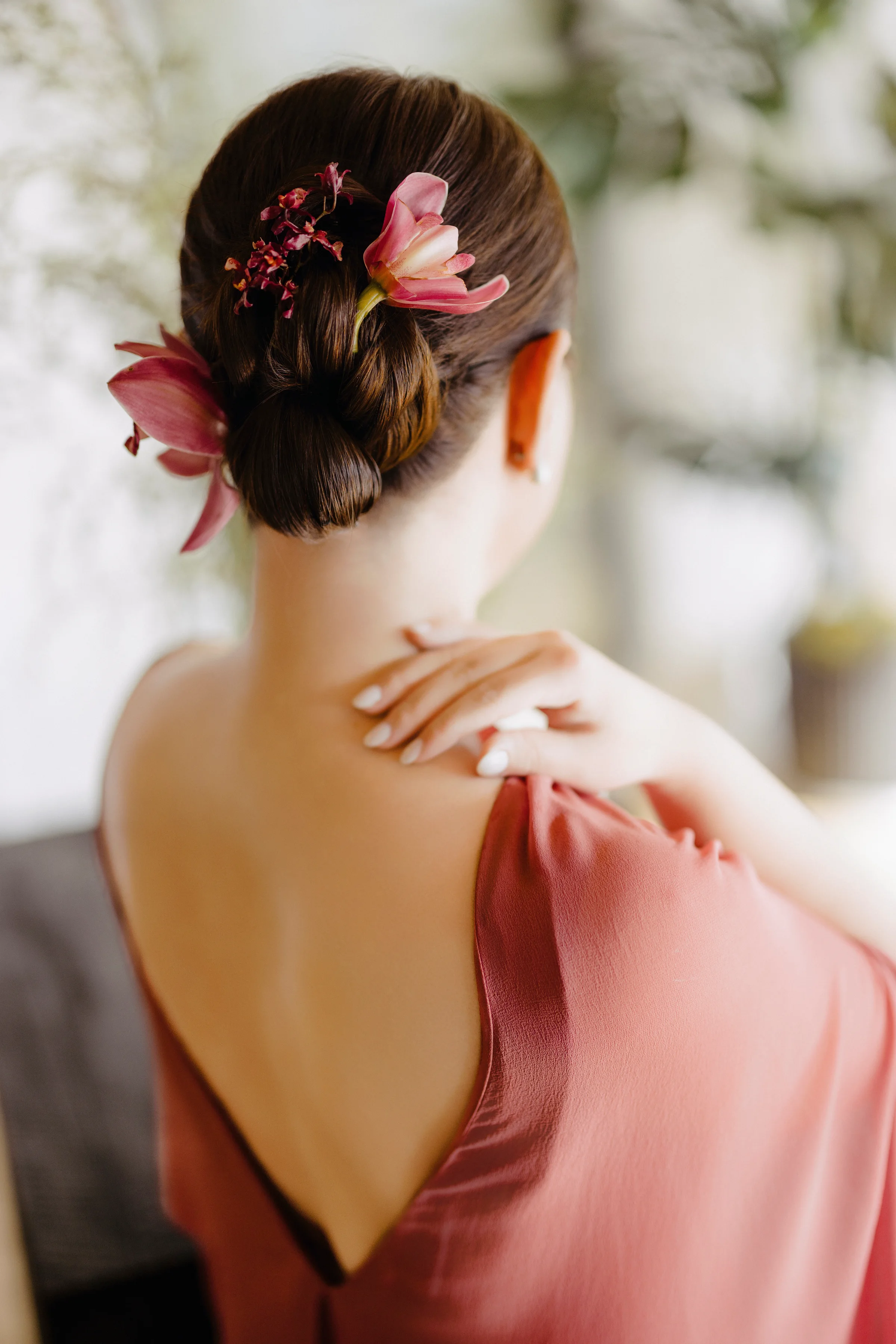Back view of the bride's coral silk dress with a red floral hairpiece in her updo