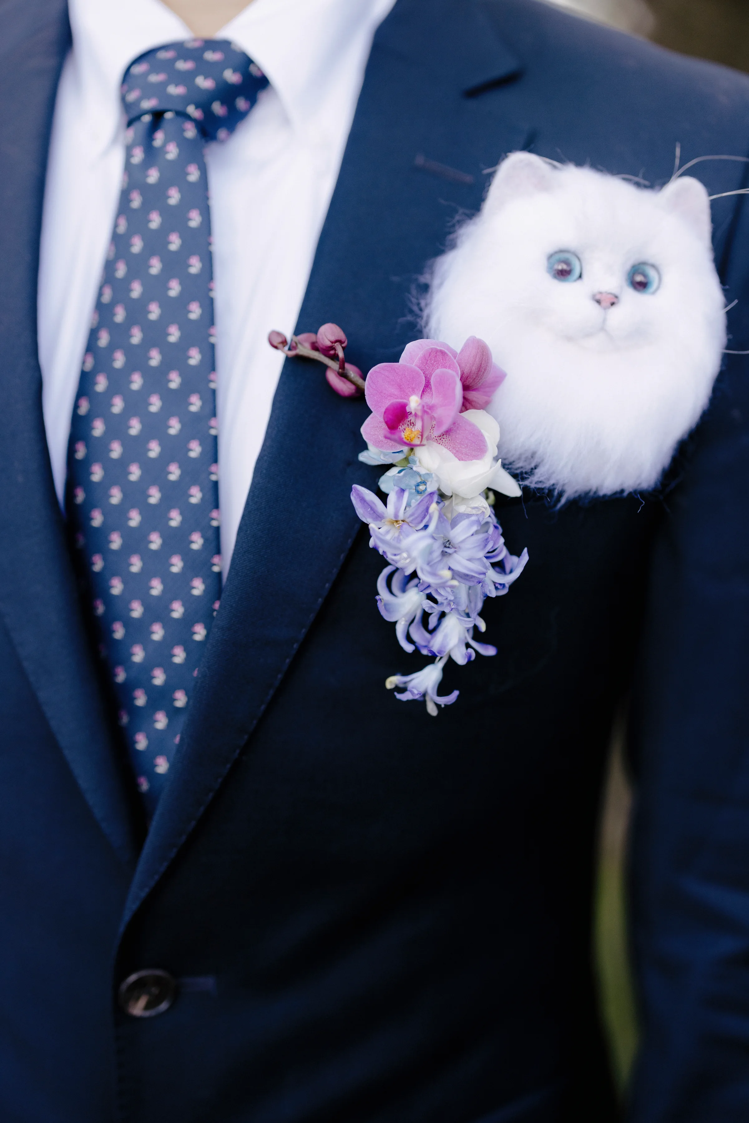 Groom's navy lapel with a boutonnière and a fluffy white cat brooch