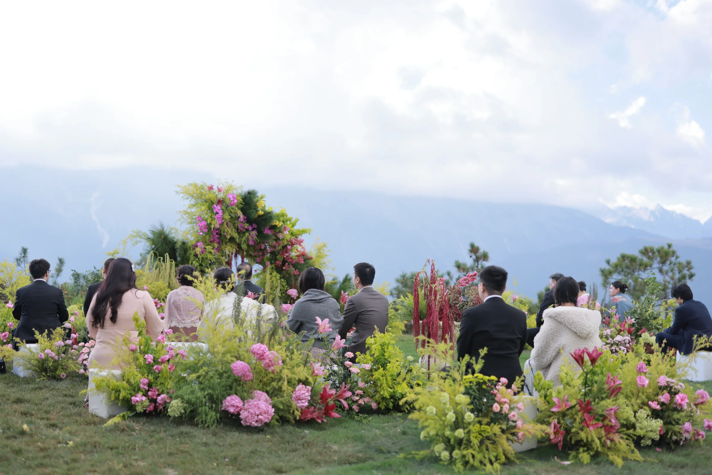 Guests seated at an outdoor ceremony framed by florals and a mountain vista