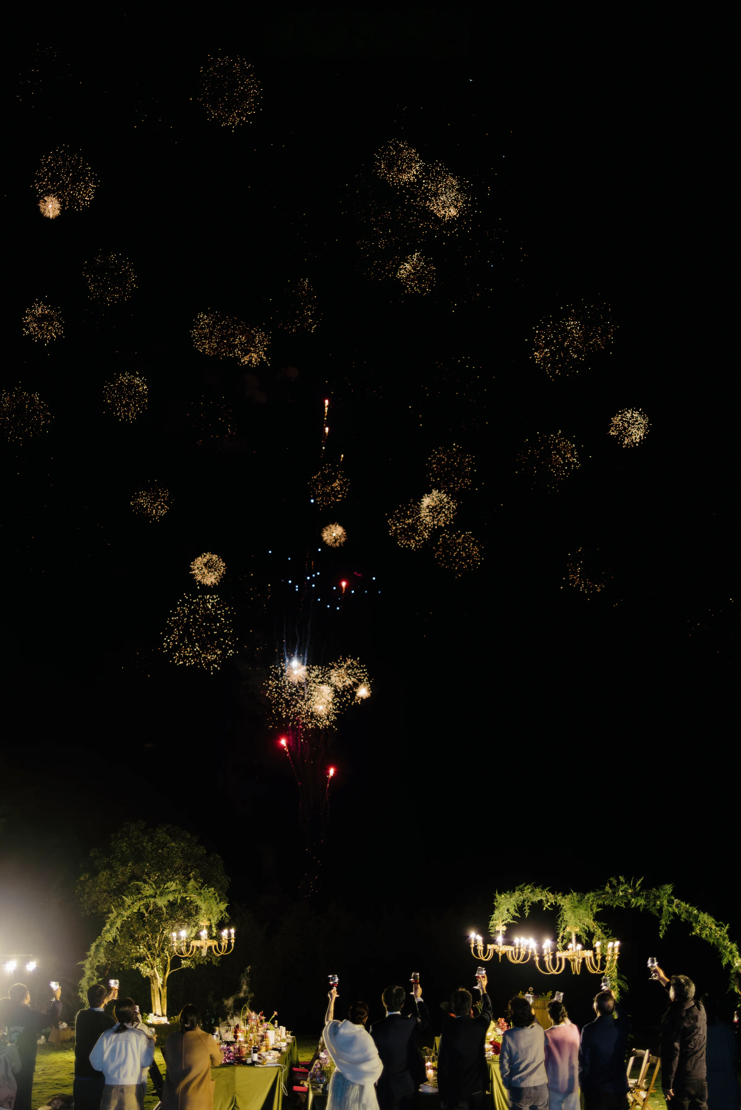 Fireworks bursting over the venue as guests watch by a floral arch