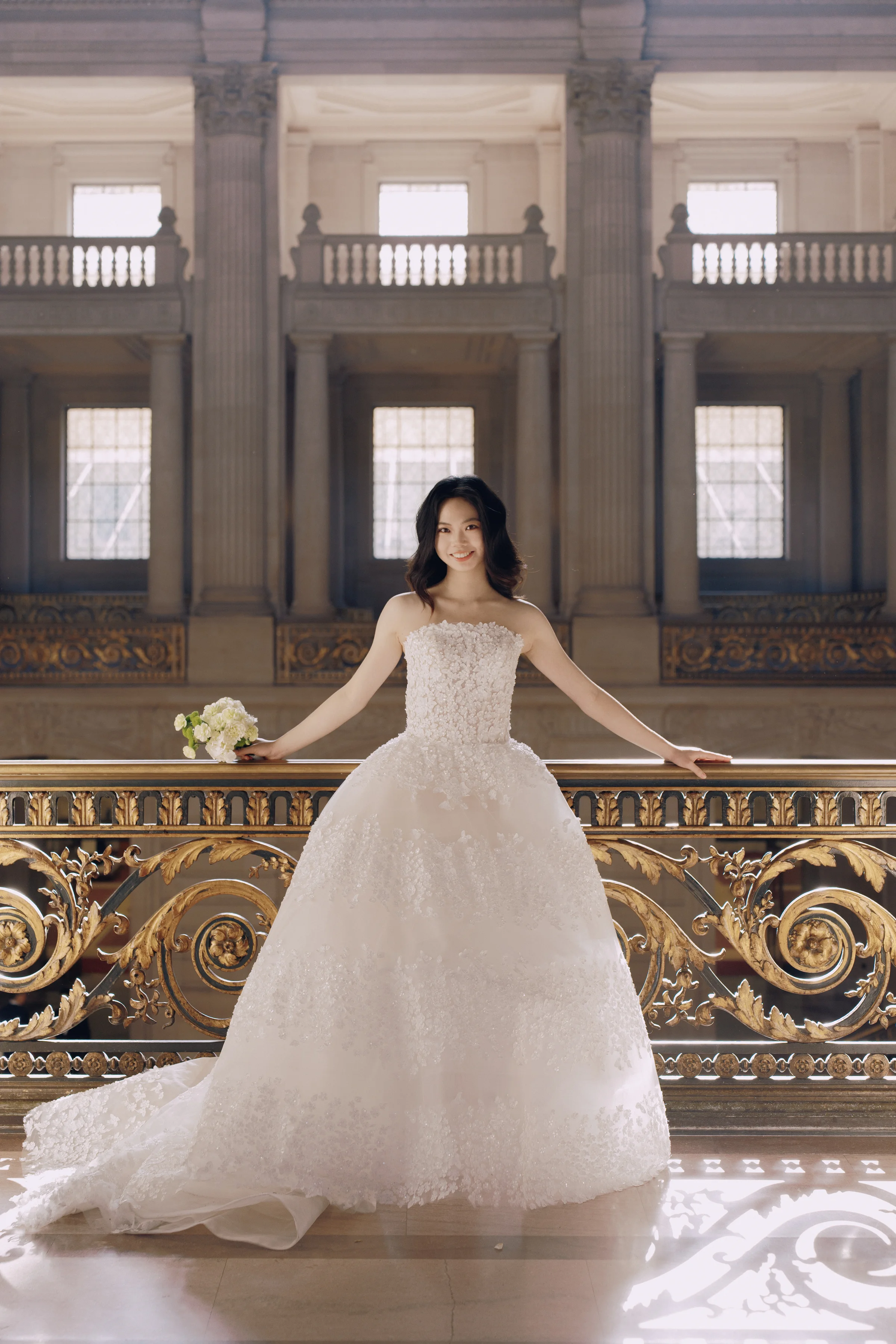Bride in her lace ballgown posing at the balustrade of the grand staircase