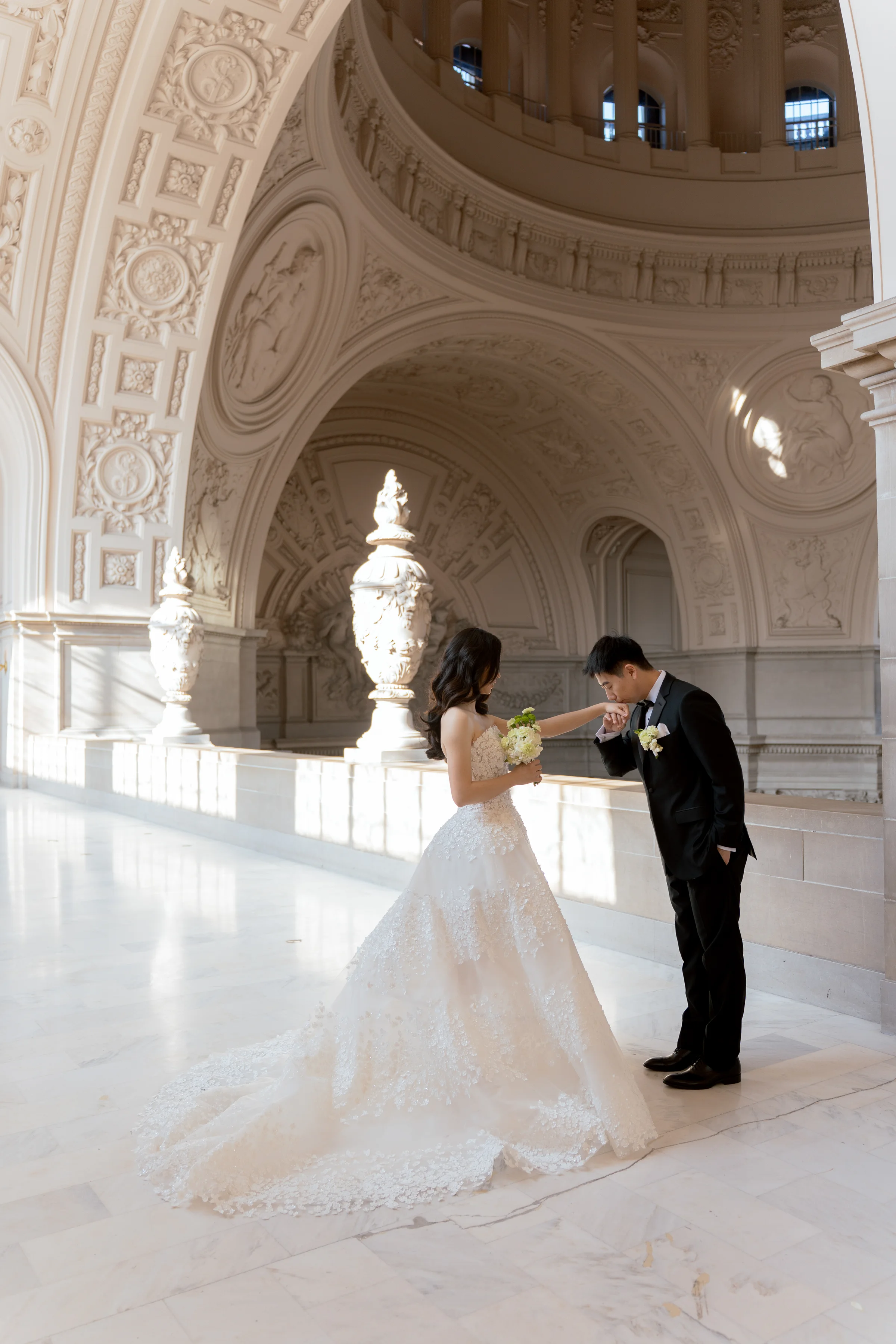 Groom kissing the bride's hand in a sunlit marble hall