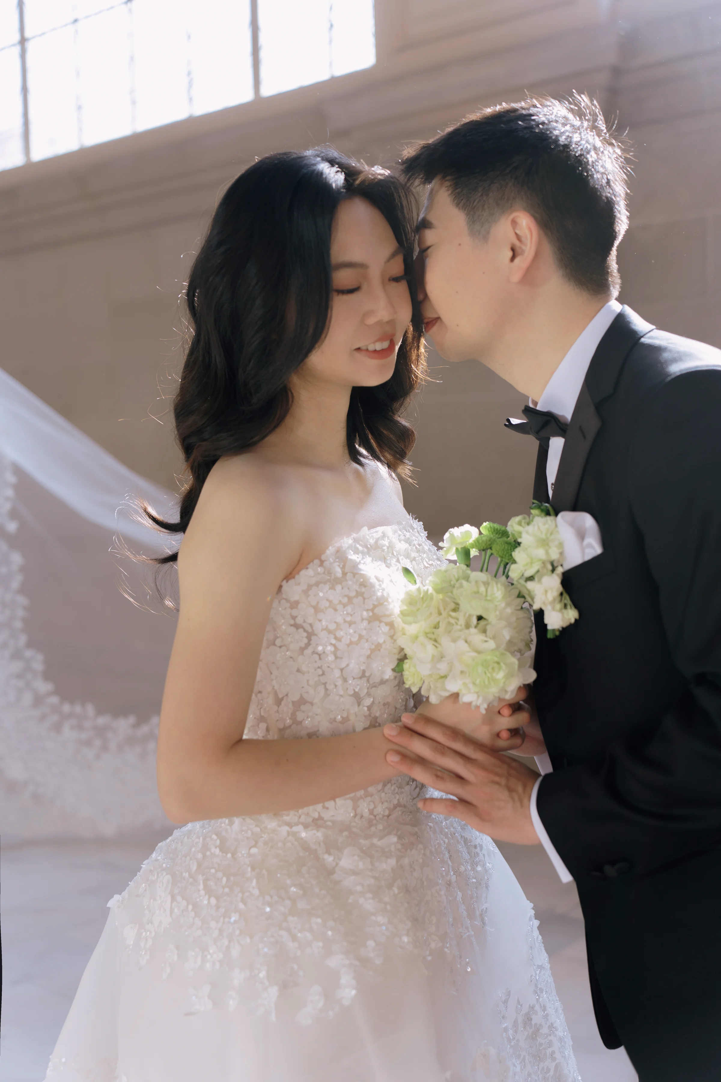 Couple with foreheads together, the bride holding a white bouquet