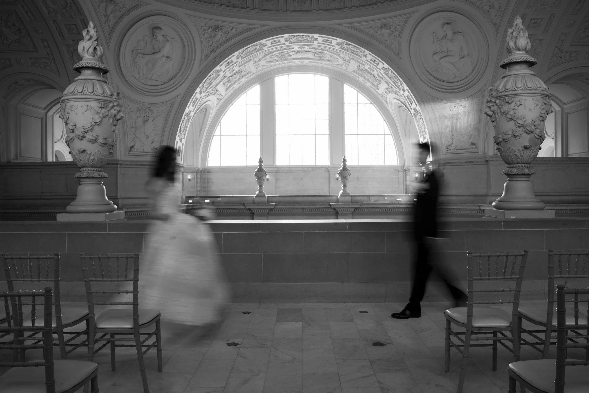 Black-and-white motion-blurred figure crossing the ceremony room by an arched window
