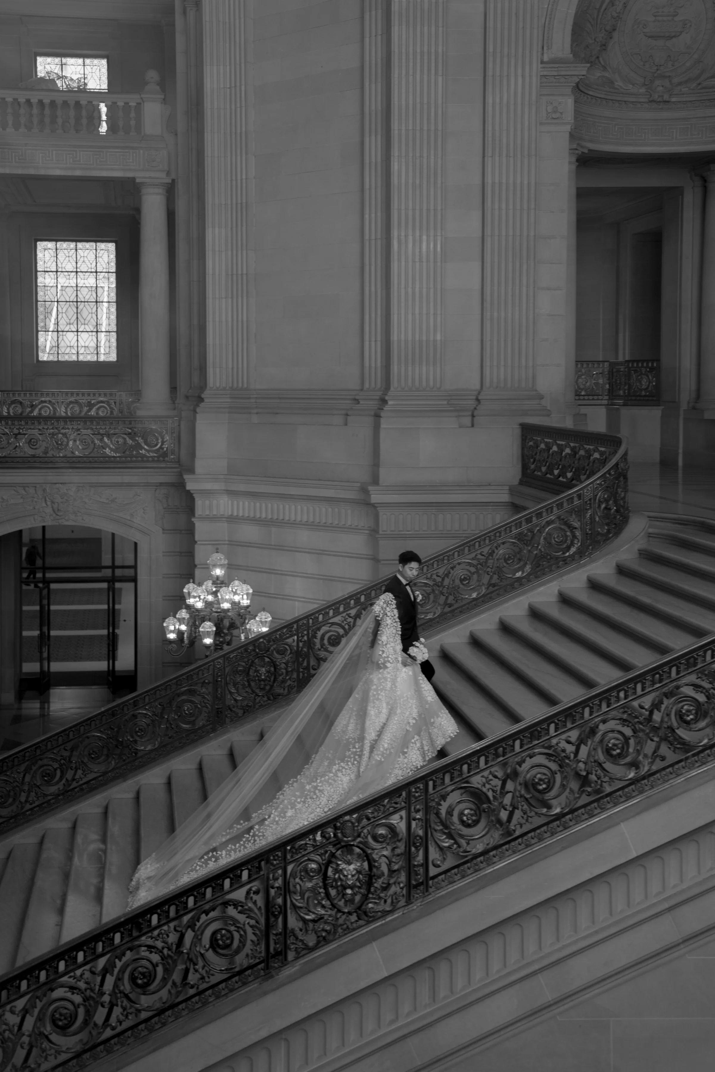 Black-and-white view of the couple on an ornate staircase, the bride's train trailing