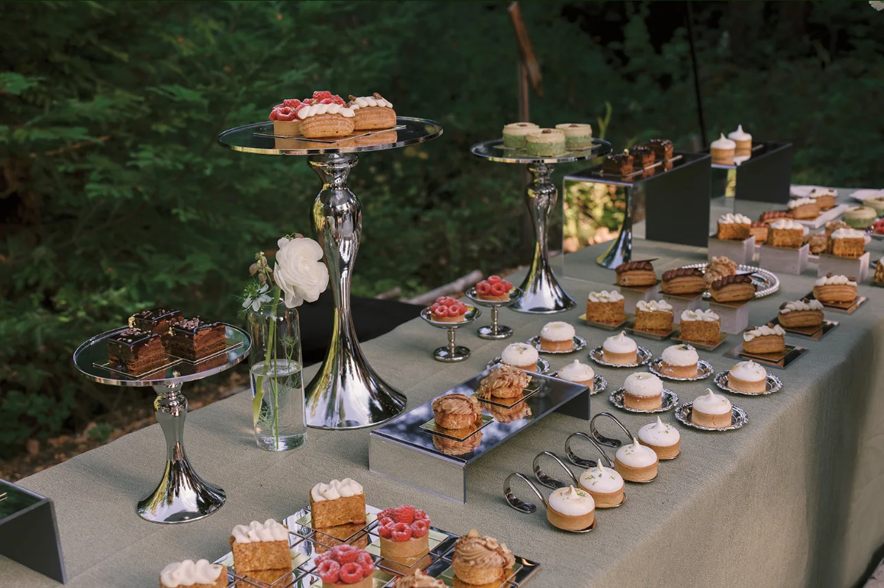 Assorted miniature cakes, tarts, and pastries displayed on mirrored stands at the woodland reception.