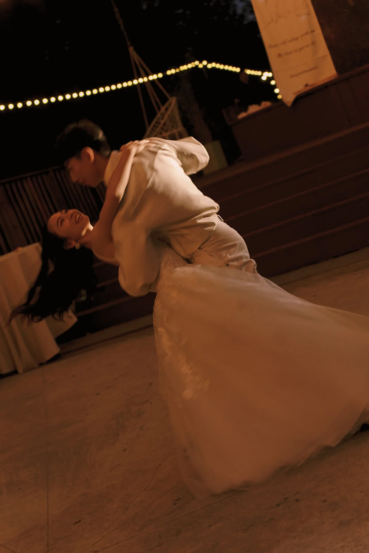 Newlyweds dancing together beneath warm string lights during the evening reception.