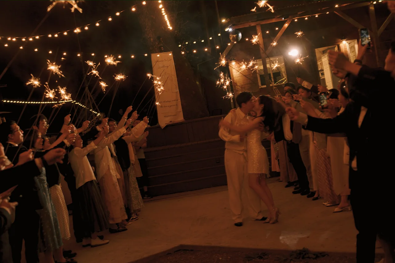 Newlyweds kissing as guests hold sparklers along both sides of the nighttime reception dance floor.