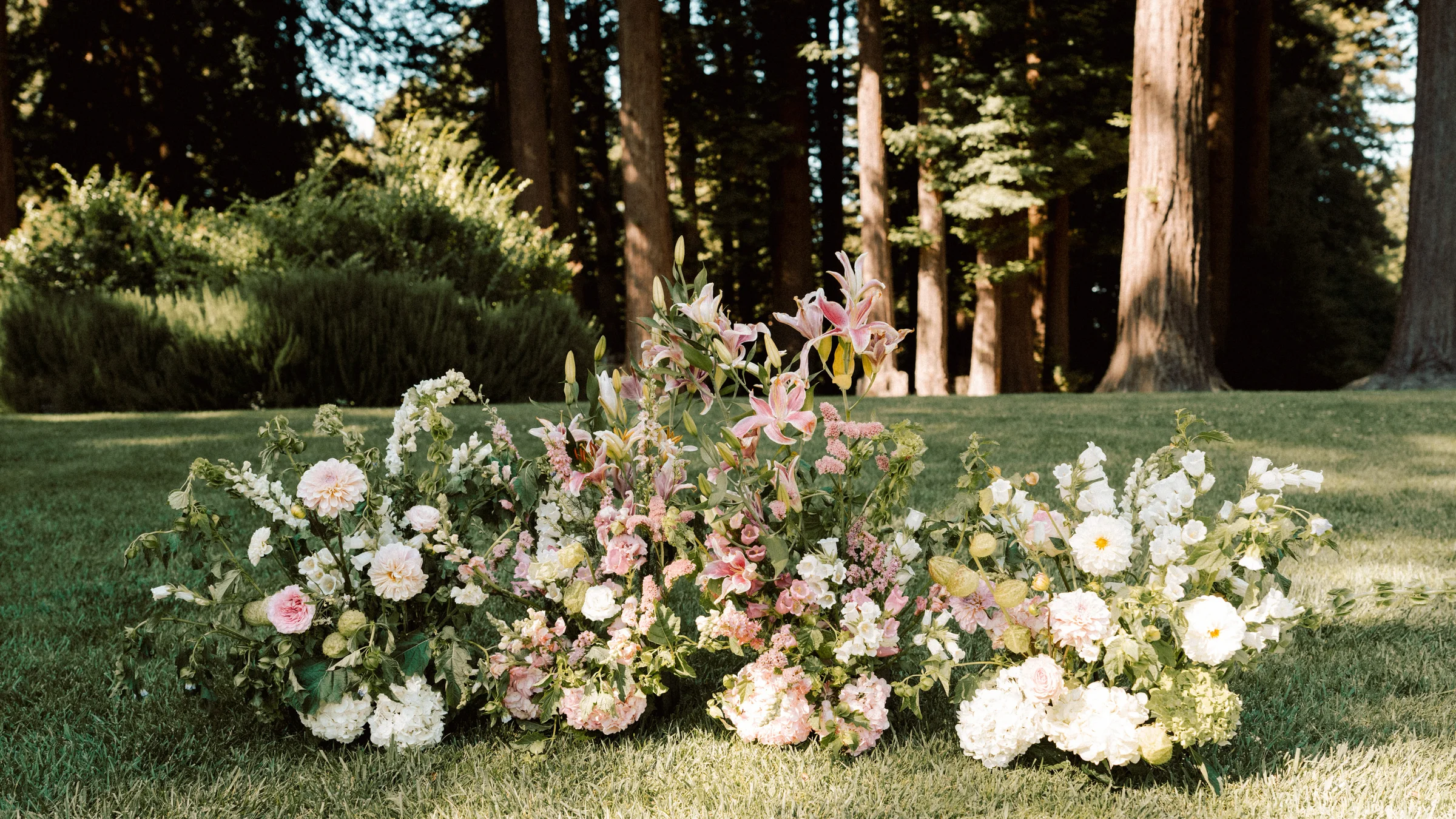 Pastel garden-style ground florals arranged on a lawn beneath redwood trees